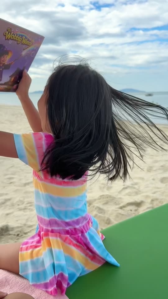 A little reader holds up her personalized Stattner storybook, The Wobbly Wand.